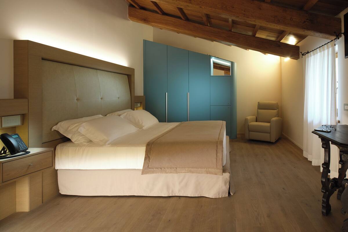 A bedroom with a bed, a chair, a desk, and a wardrobe.