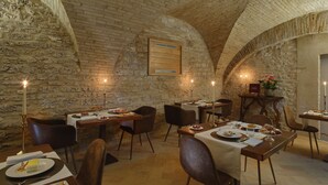 A rustic dining area with stone walls and vaulted ceilings, featuring tables set with plates of food and candles. - Ascesi Resort (Assisi)