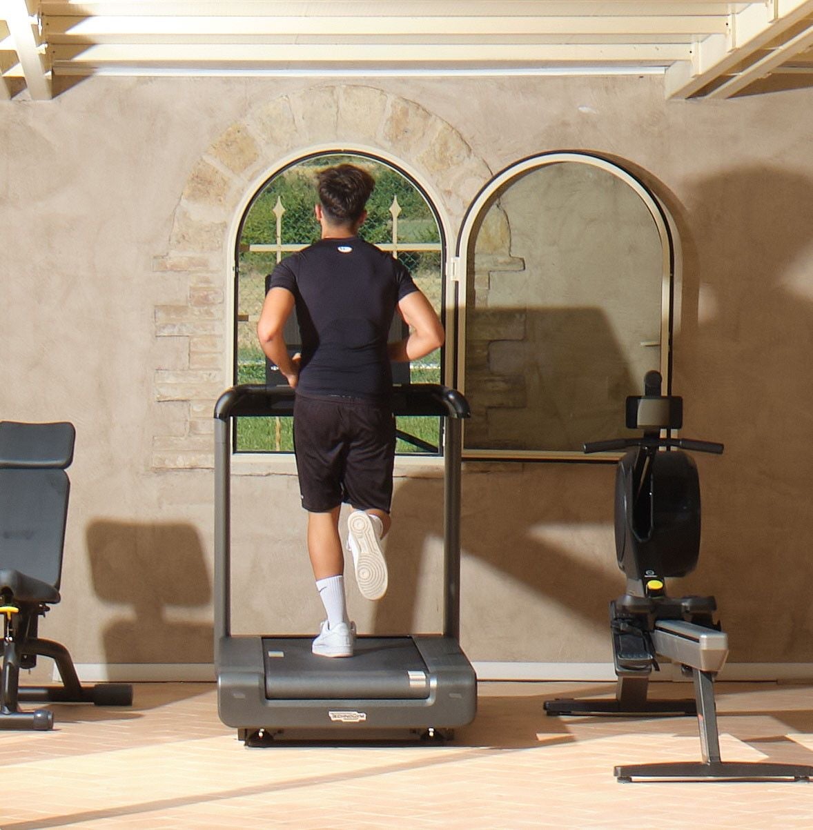 Una persona usando una cinta de correr en una habitación con pared de piedra y ventana.