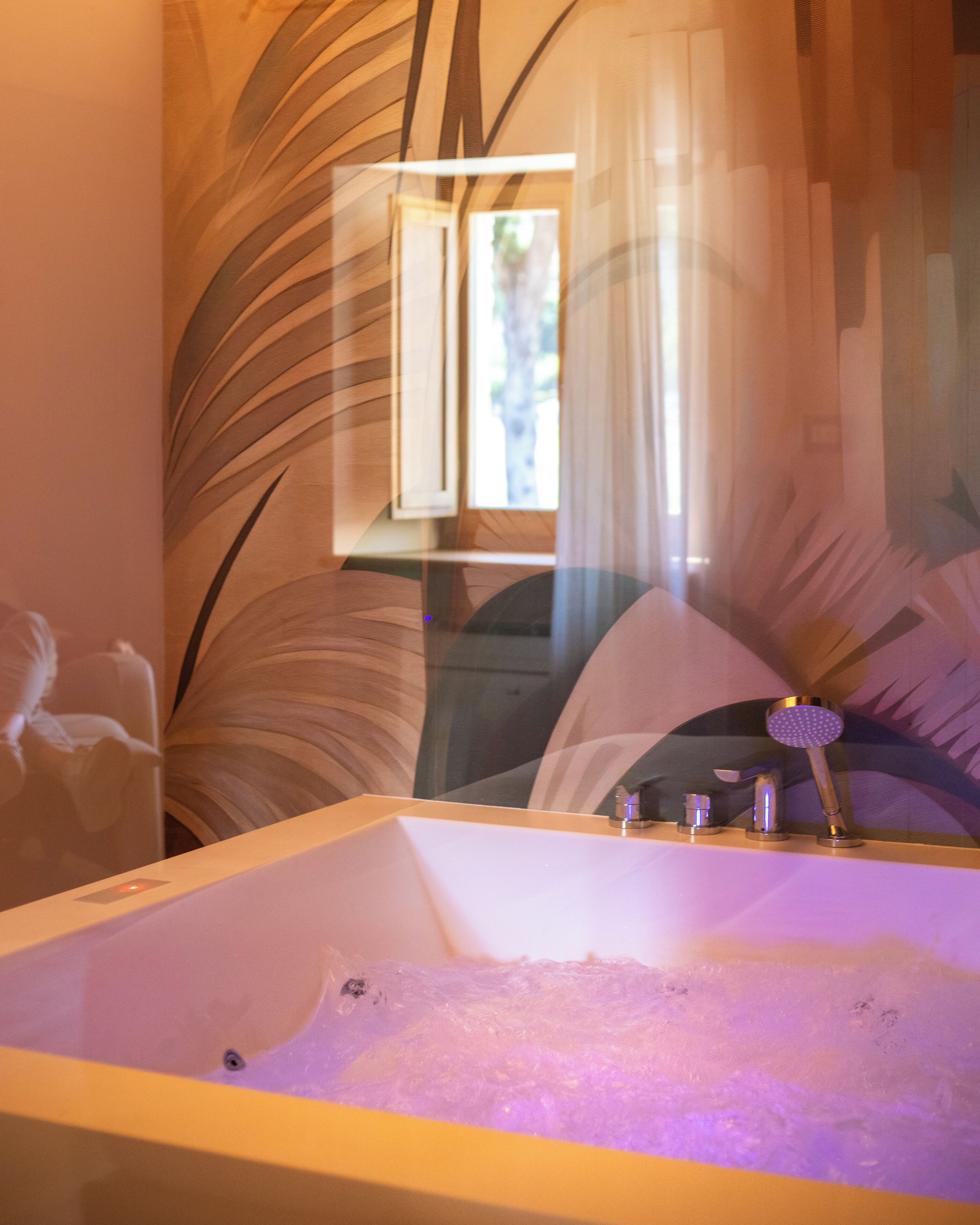 Un baño moderno con una bañera independiente, un cabezal de ducha y una ventana con cortinas traslúcidas.