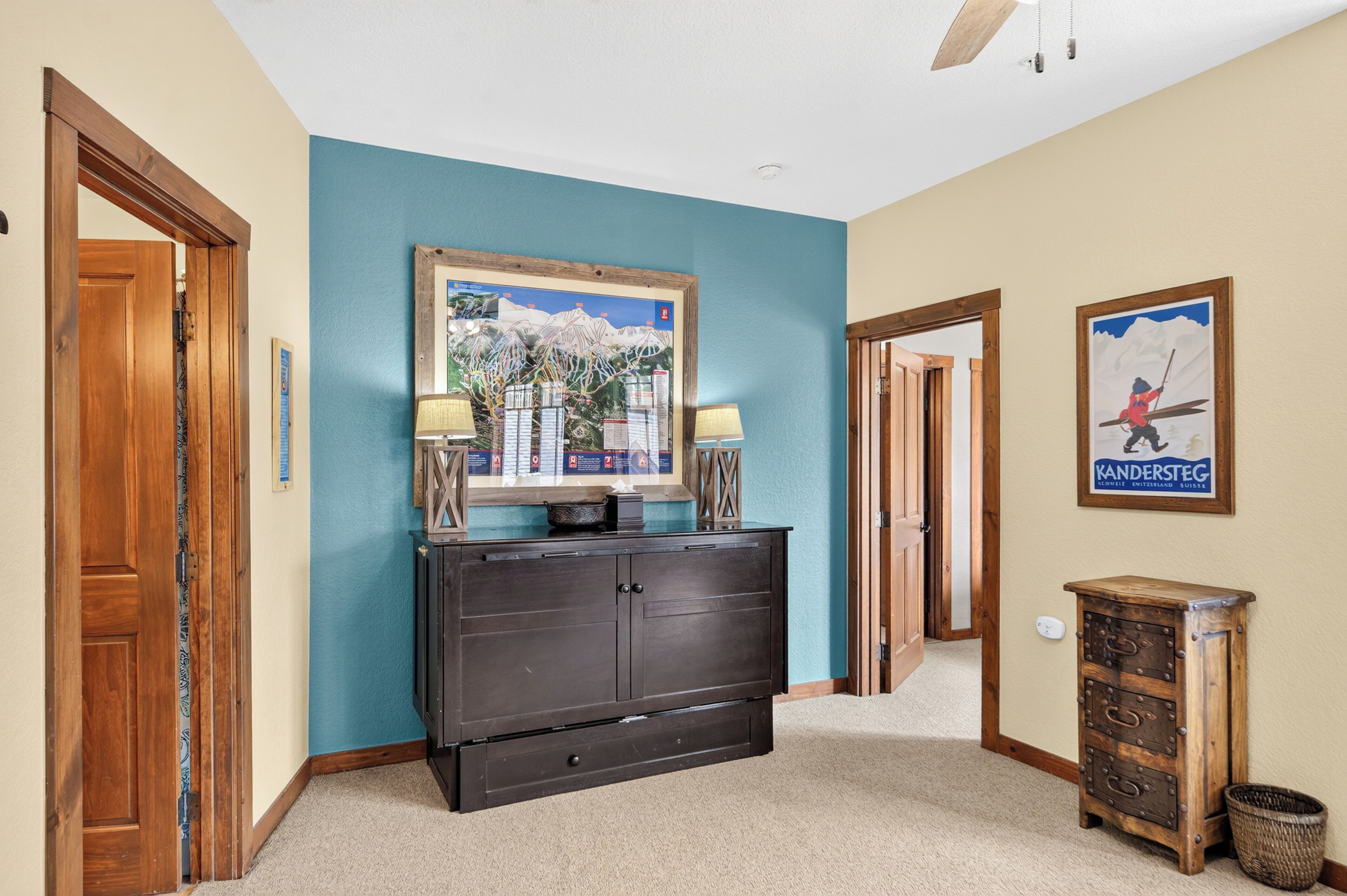 A hallway with a dark wooden cabinet, a framed map on the wall, and a poster of a skier.