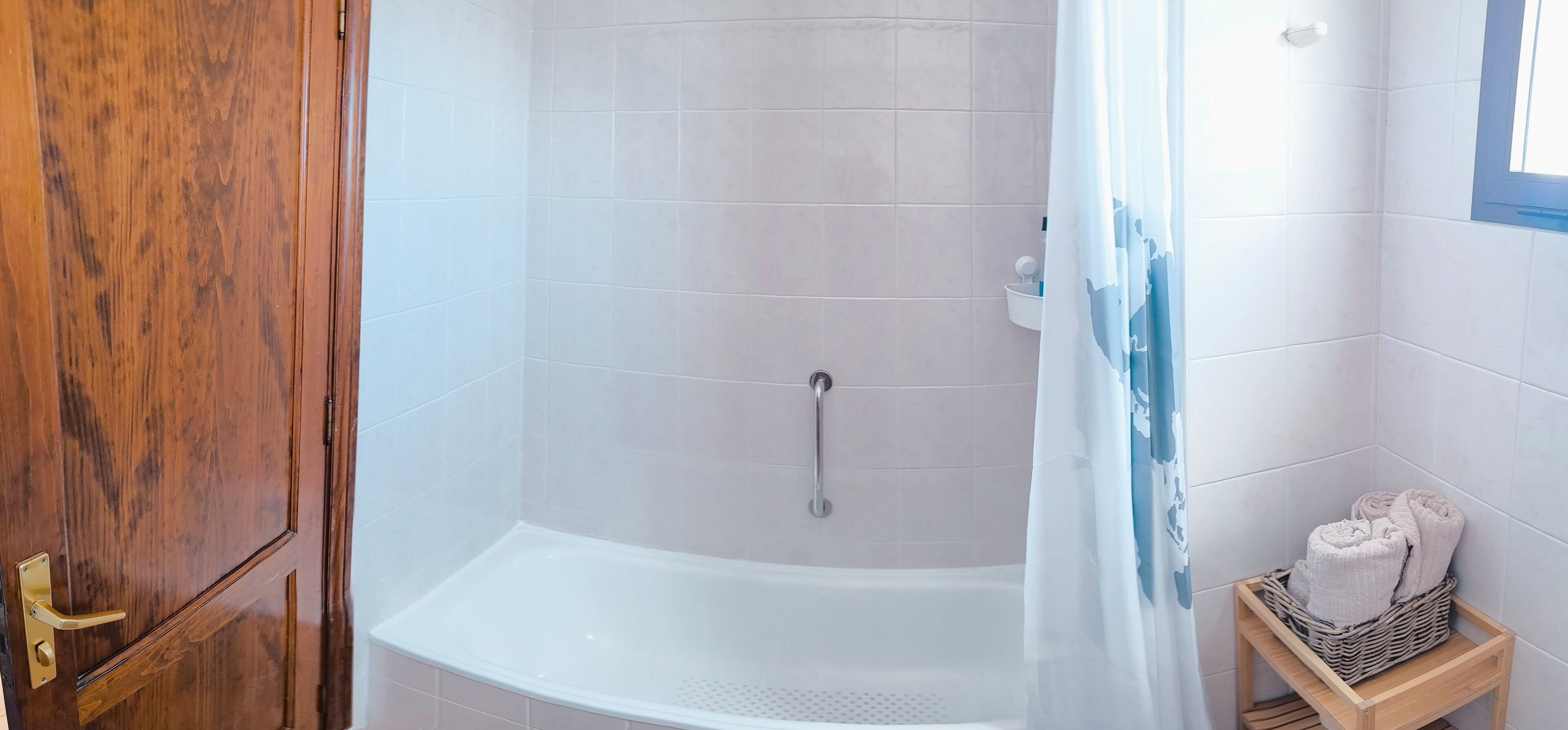A bathroom with a shower, a wooden door, and a small wicker basket with towels.