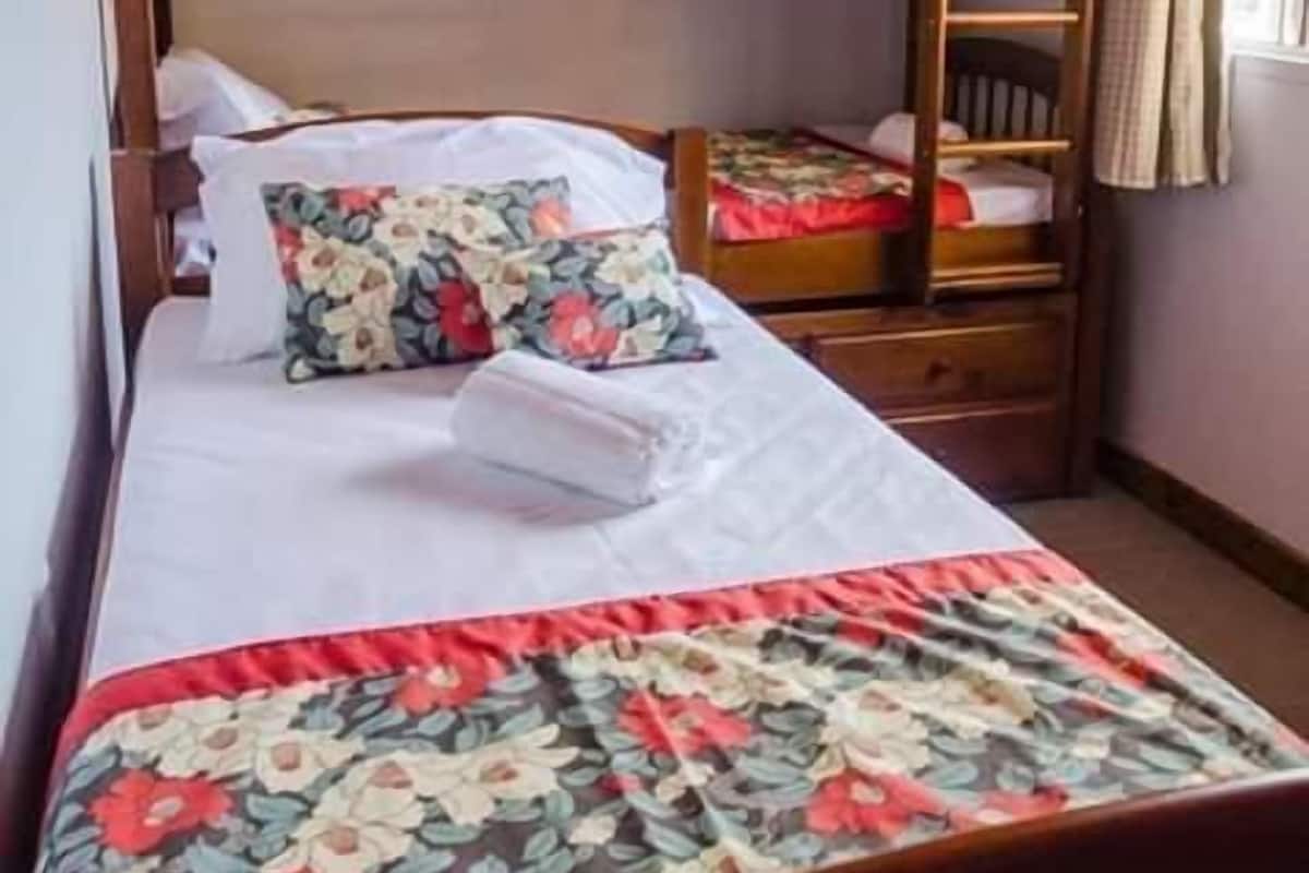 A bunk bed room with a wooden headboard, a floral bedspread, and a window with curtains.