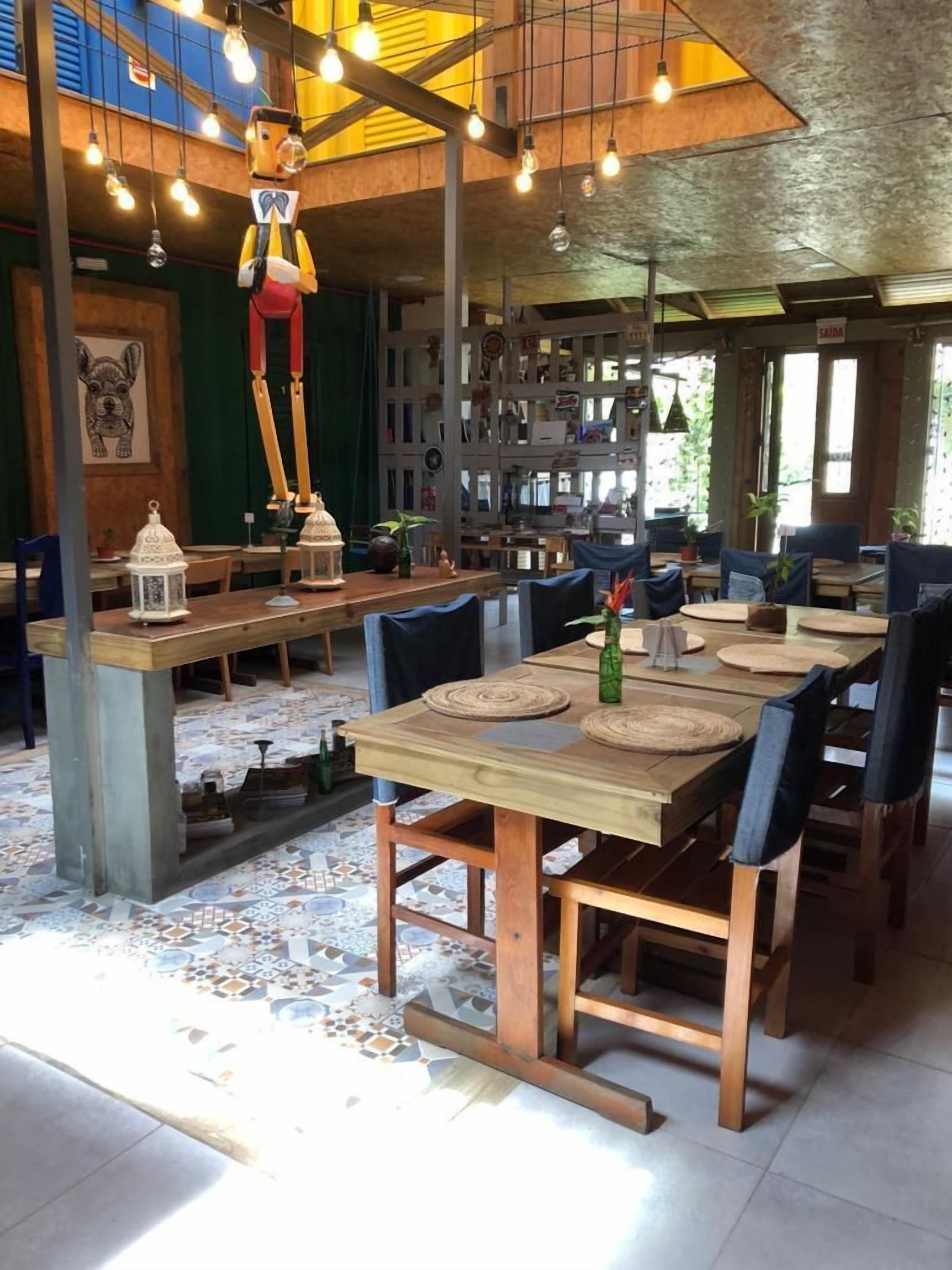 Ein Restaurant mit Holztischen und -stühlen, hängenden Lampen und einem gefliesten Boden.