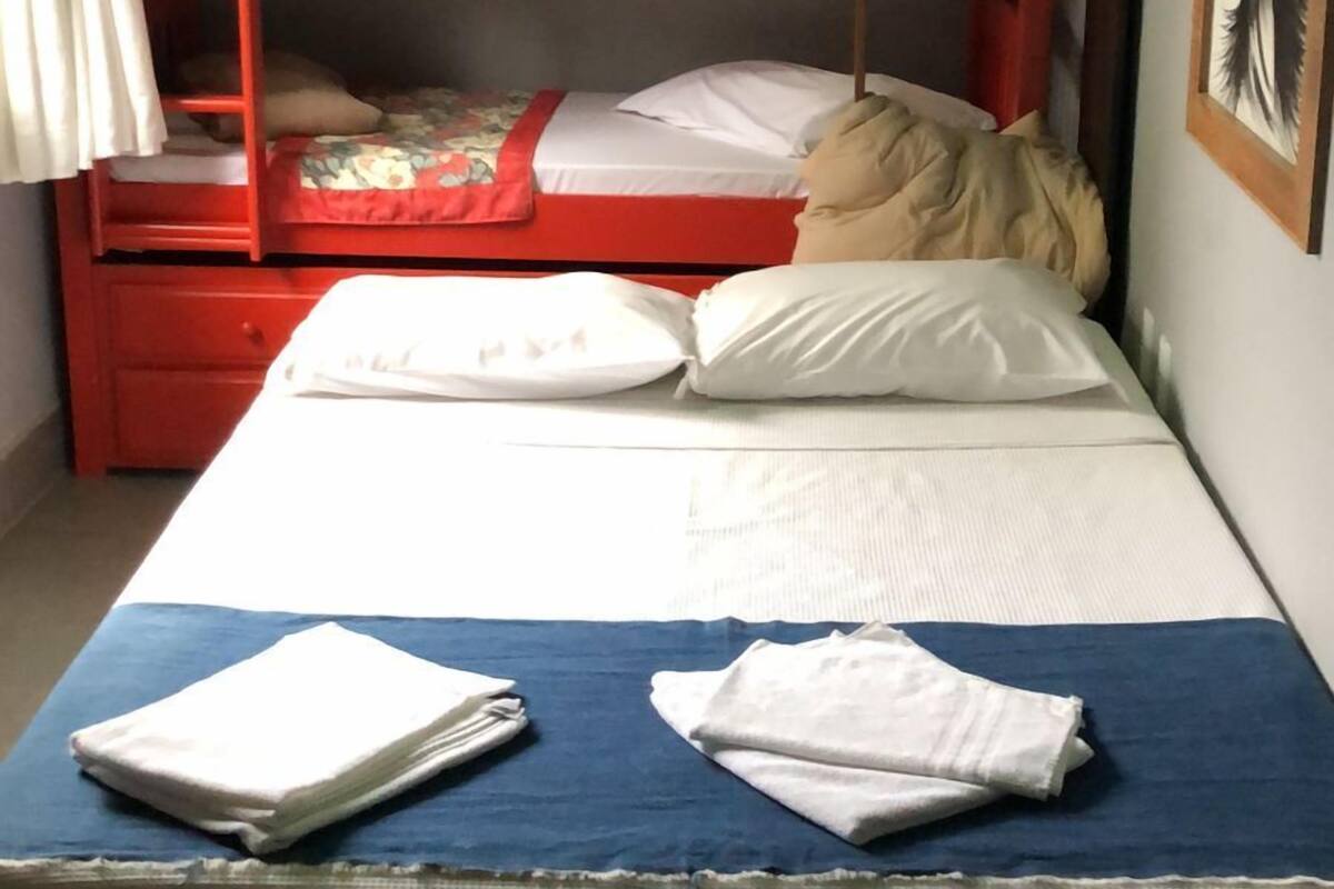 A bunk bed with a red frame, white bedding, and a blue bedspread. There is a white air conditioning unit on the wall and a framed picture on the wall.