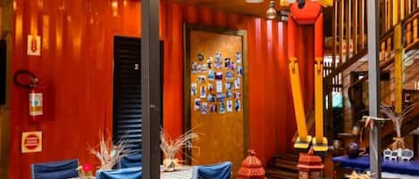 A restaurant with wooden tables, blue chairs, hanging light fixtures, and a red wall with a mural.