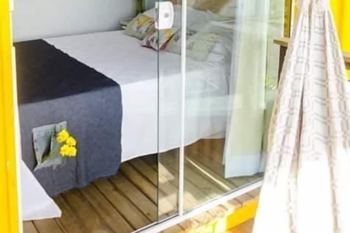 A room with a bed, a small table with a plant, and a glass door leading to an outdoor area.