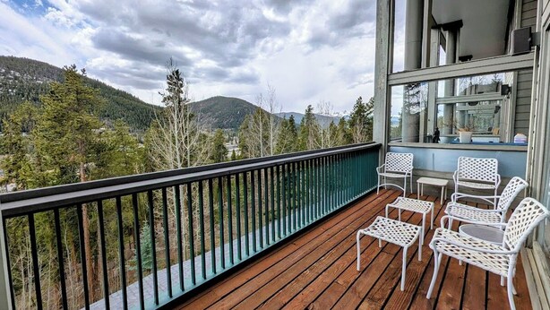 A wooden deck with white wicker chairs and a table, overlooking a mountainous landscape. - Mountain views, spacious, trails, shared hot tub (Keystone)
