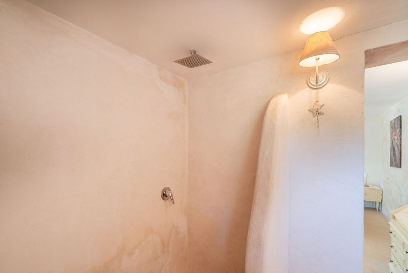 Une salle de bain avec une douche, un luminaire fixé au mur et une poignée de porte visible.