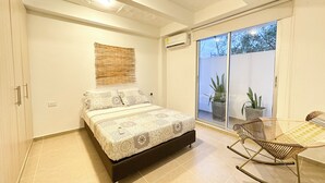A bedroom with a bed, a rocking chair, a potted plant, and a sliding glass door leading to an outdoor area.