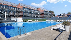 Ein Schwimmbecken mit Liegestühlen und ein Gebäude mit mehreren Balkonen im Hintergrund.