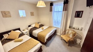 A hotel room with two beds, a chair, a window with curtains, and a small table with cups and a kettle. - AYSGARTH HOUSE (Blackpool)