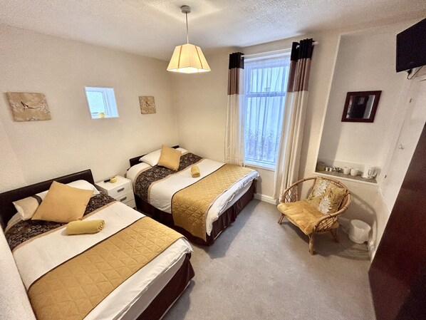 A hotel room with two beds, a chair, a window with curtains, and a small table with cups and a kettle. - AYSGARTH HOUSE (Blackpool)