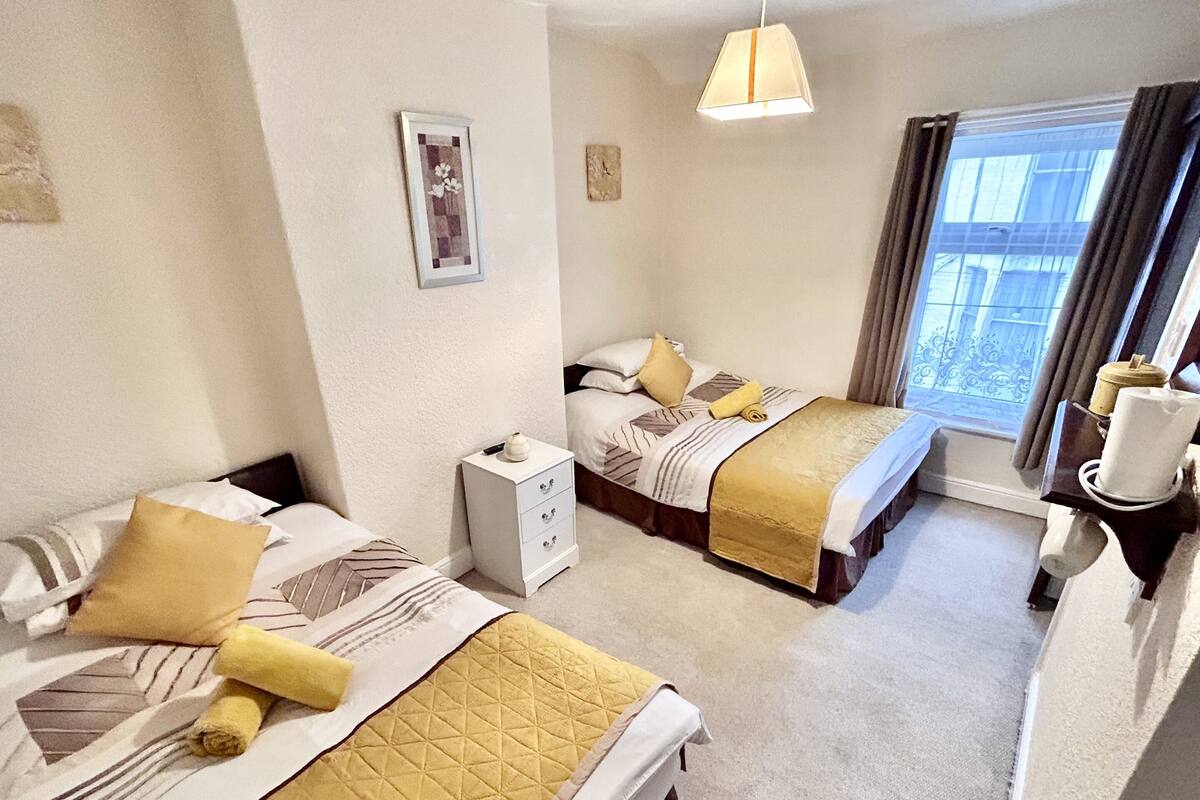 Una habitación de hotel con dos camas, una mesita de noche pequeña, una lámpara colgante y una ventana con cortinas.