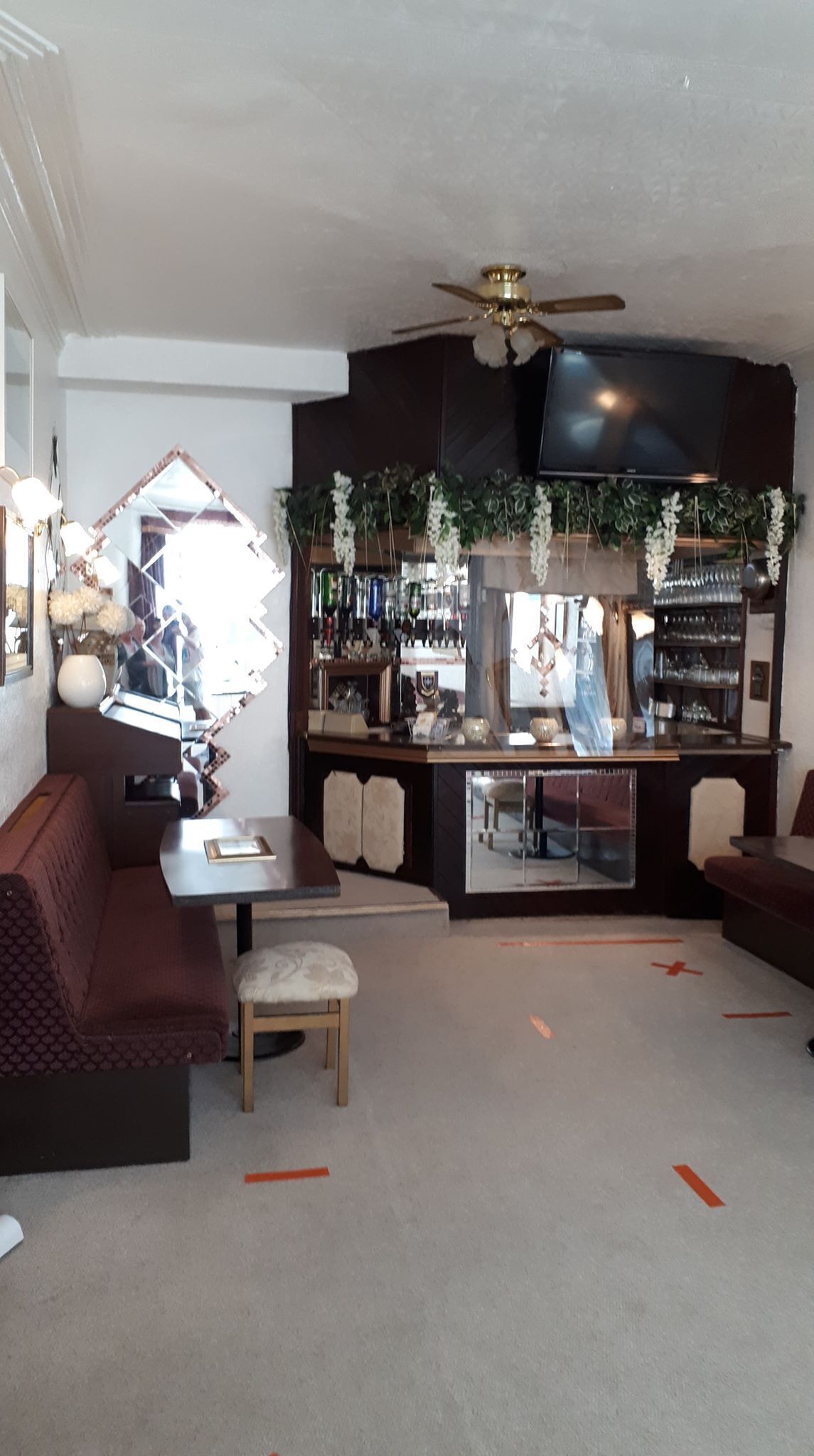 A cozy living room with a brown sofa, a small table, and a chair. There is a bar area with shelves of bottles and a television above.