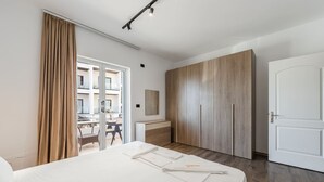 Una habitación de hotel moderna con una cama grande, un armario de madera y un balcón con vistas a la ciudad.