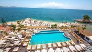 Zona de piscina en un resort con tumbonas y sombrillas, una piscina grande y vistas al mar.