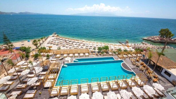A resort pool area with sun loungers and umbrellas, a large pool, and a view of the sea. - Saranda Beach Living - 1BR Apartment (Sarandë)