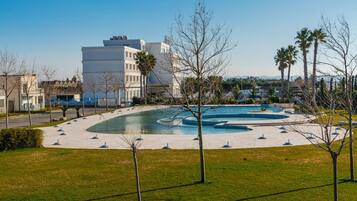 Un edificio moderno con un patio que incluye una fuente circular y palmeras.