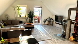 Un loft moderno con techo alto, un sofá, un televisor, una chimenea y vistas por la puerta abierta.