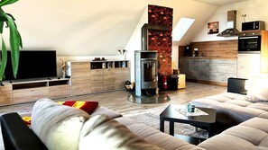 A modern living room with a fireplace, a television, and a kitchen area. - Apartment 'Goldach' with Balcony and Wi-Fi (Hallbergmoos)