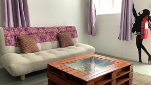 Un salon comprenant un canapé, une table basse avec un plateau en verre et un extincteur fixé au mur.