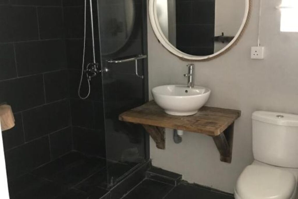 A bathroom with a glass-enclosed shower, a white sink on a wooden shelf, and a toilet.