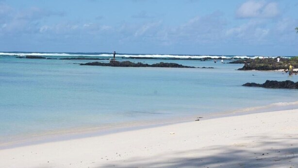 Une plage à l’eau claire, avec un promontoire rocheux et une rive sablonneuse.