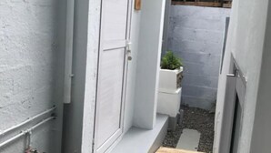 Une ruelle étroite avec une porte blanche, un petit bac à fleurs orné de plantes vertes et un banc en bois.