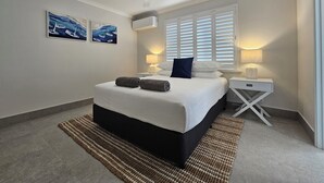 Un dormitorio ordenado con cama, lámparas de noche, ventilador de techo y obras de arte en la pared.