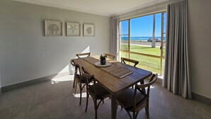 Un comedor con una mesa grande y sillas, una lámpara en el techo y vistas a la playa a través de amplias ventanas.