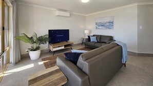 Una sala de estar moderna con un televisor de pantalla plana, un sofá, una mesa de centro, una planta en maceta y un cuadro en la pared.