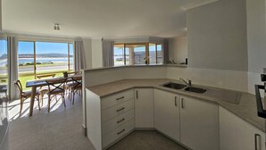 Una cocina moderna con vista a la playa, un comedor con mesa y sillas, y un amplio ventanal.