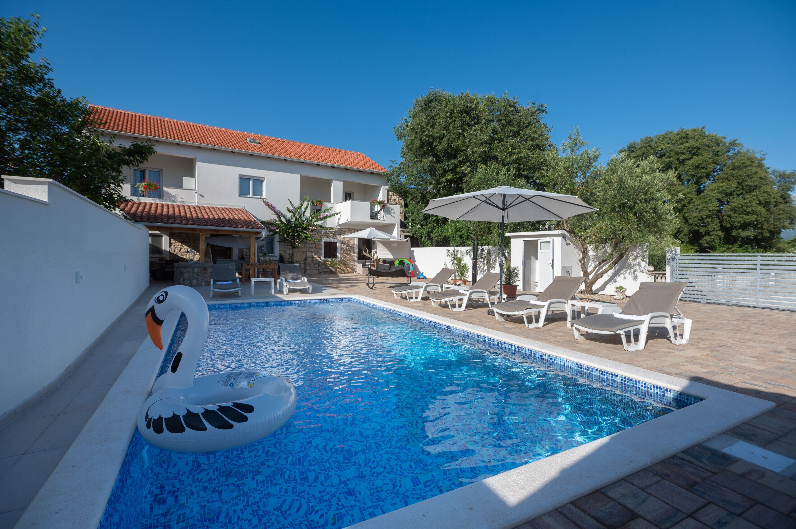 Une piscine avec un flotteur en forme de cygne, des chaises longues et des parasols.