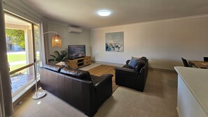 Ein modernes Wohnzimmer mit einer Couch, einem Couchtisch, einem Fernseher auf einem Holzständer und einem Gemälde an der Wand.