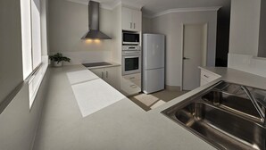 Una cocina moderna con armarios blancos, un lavamanos de acero inoxidable y electrodomésticos integrados, incluyendo un refrigerador y horno.