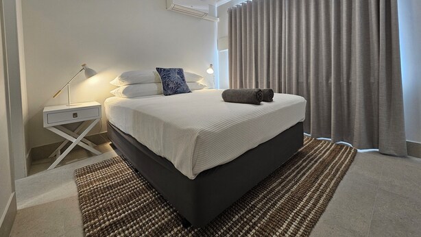 Un dormitorio con cama, mesitas de noche, ventilador de techo y una ventana con cortinas.