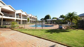 Un edificio residencial con piscina, patio cercado y césped bien cuidado.