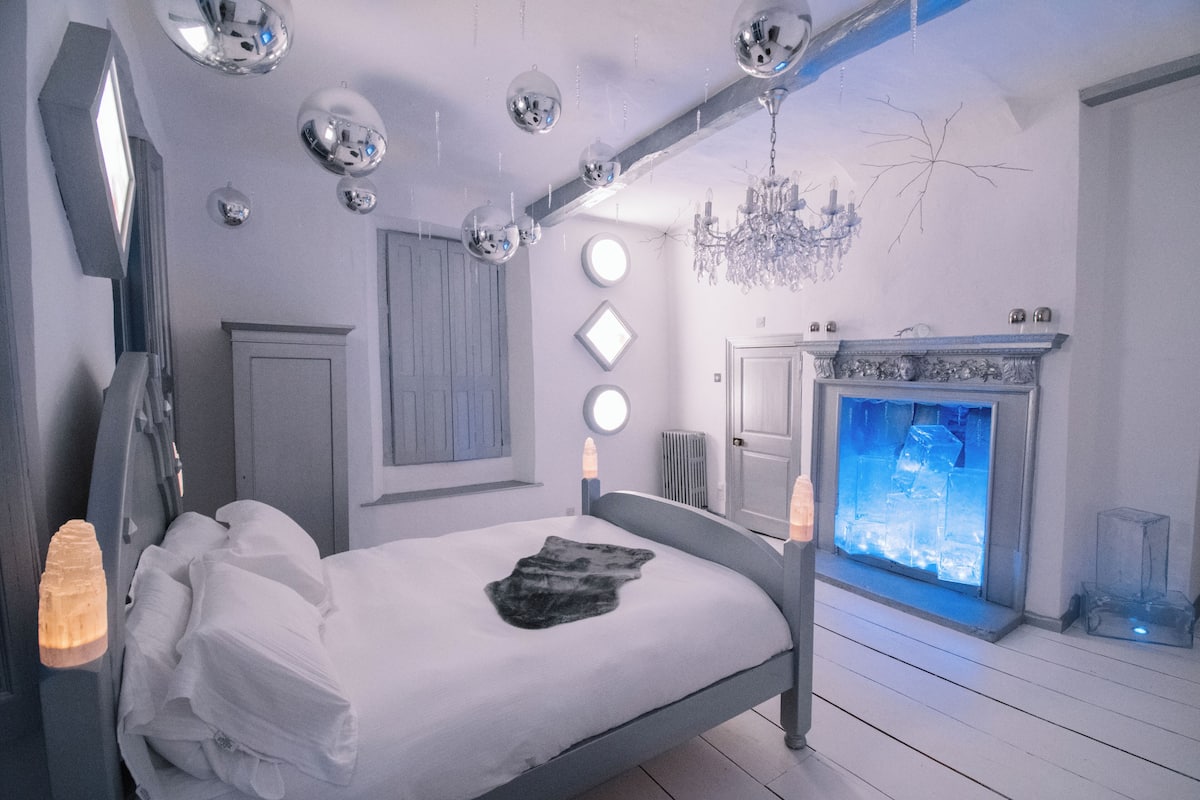 Une chambre à coucher avec un lit, un lustre, une cheminée et des miroirs décoratifs.