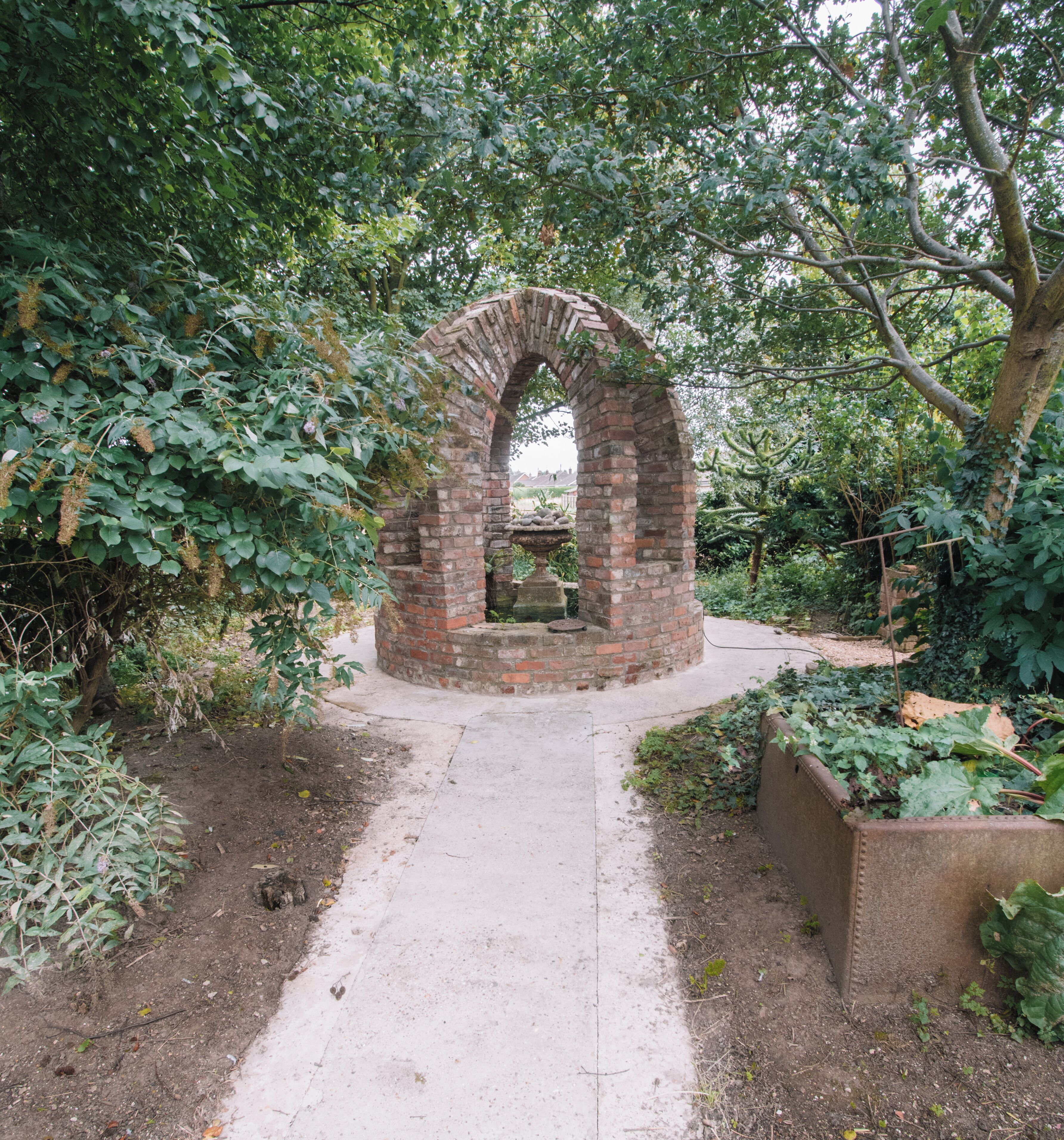 A brick archway with a small table at its base, surrounded by greenery.