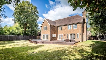 A two-story brick house with a large deck and a fenced yard.