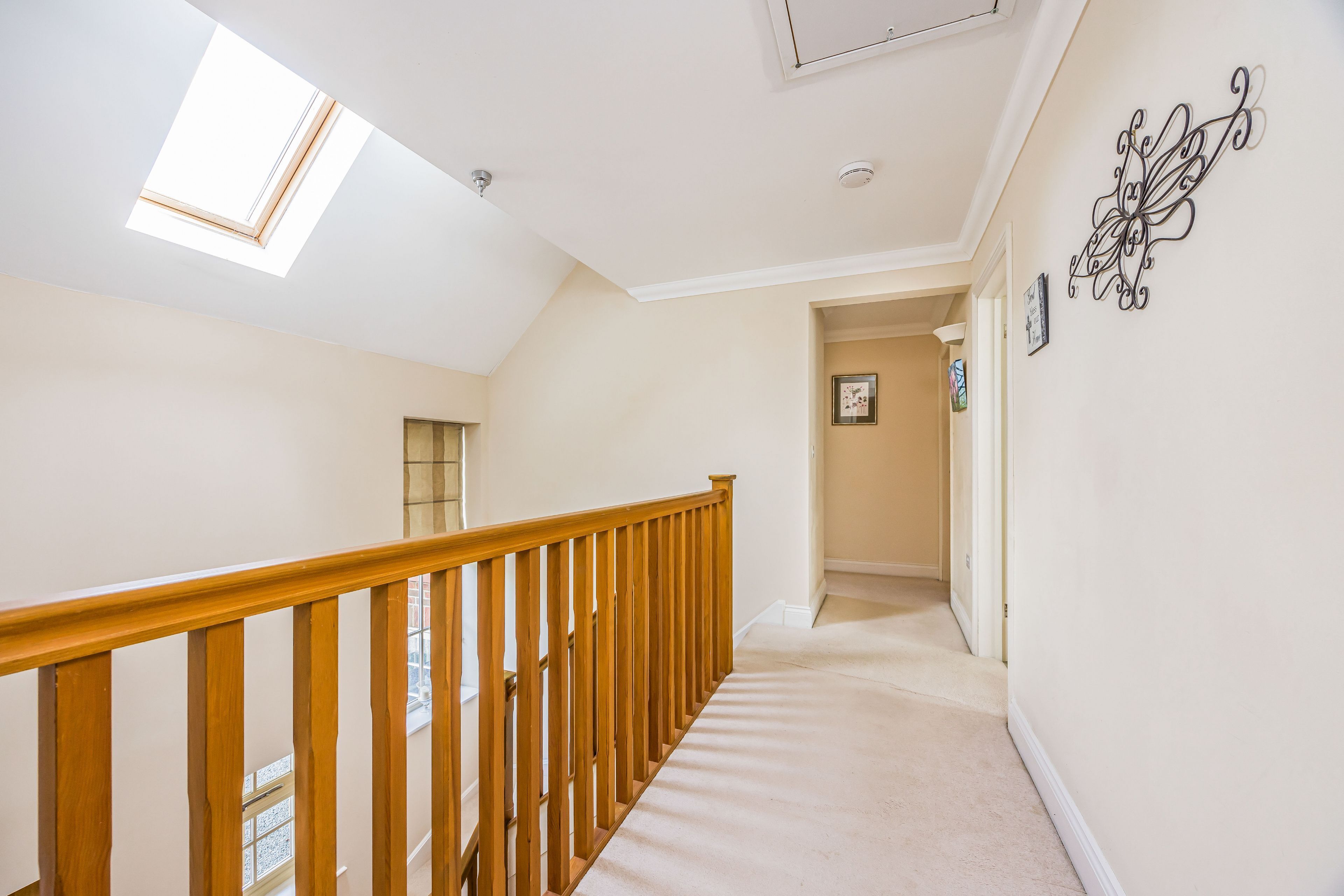 A hallway with a wooden railing, a skylight, and a wall-mounted decorative piece.
