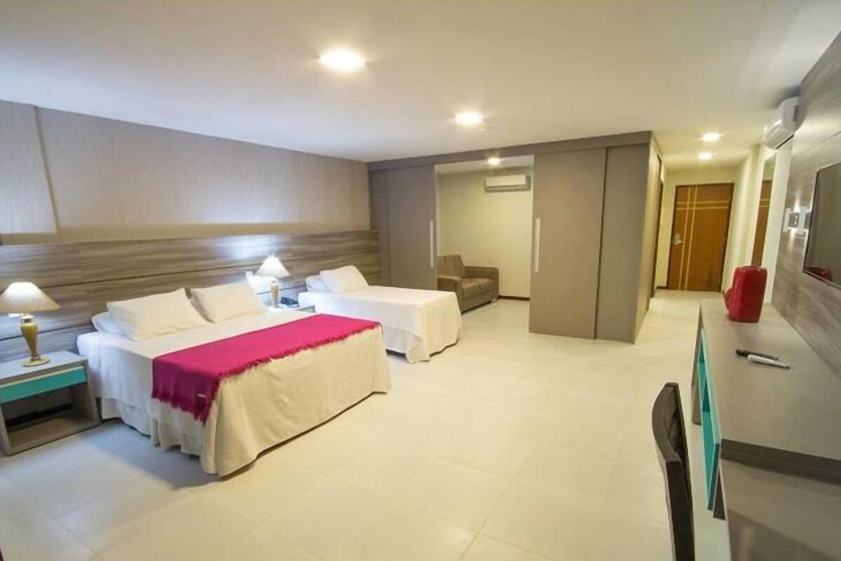 Ein Hotelzimmer mit zwei Betten, einem Schreibtisch, einem Sessel, einem Fernseher und einem Kleiderschrank.
