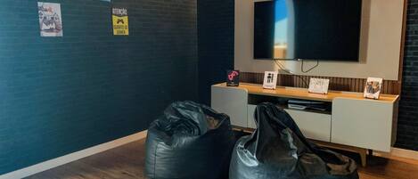 A modern room with a flat-screen TV mounted on the wall, wooden flooring, and black bean bags.