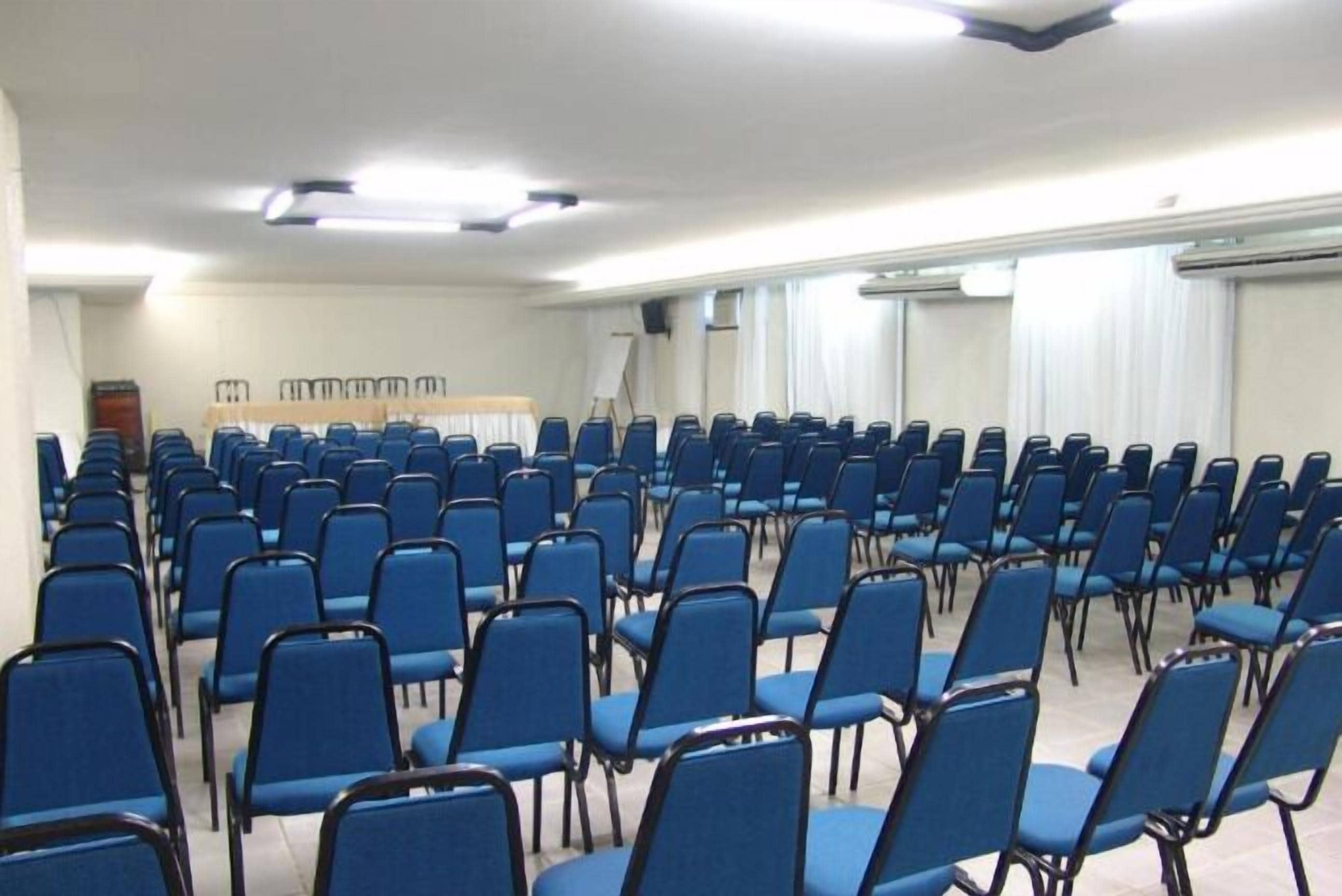 A conference room with rows of blue chairs, a whiteboard, and a projector screen.