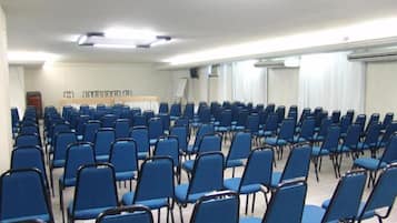 Uma sala de conferência com fileiras de cadeiras azuis, um quadro branco e uma tela de projetor.