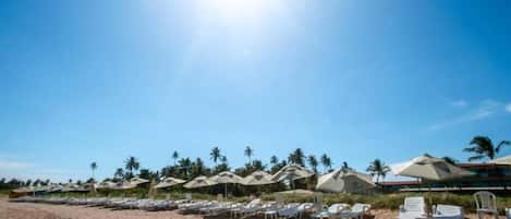 A beach with rows of white lounge chairs and thatched-roof umbrellas, suggesting a resort setting.