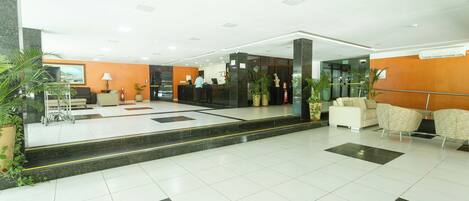 Un vestíbulo de hotel con mostrador de recepción, zona de estar y plantas en macetas.