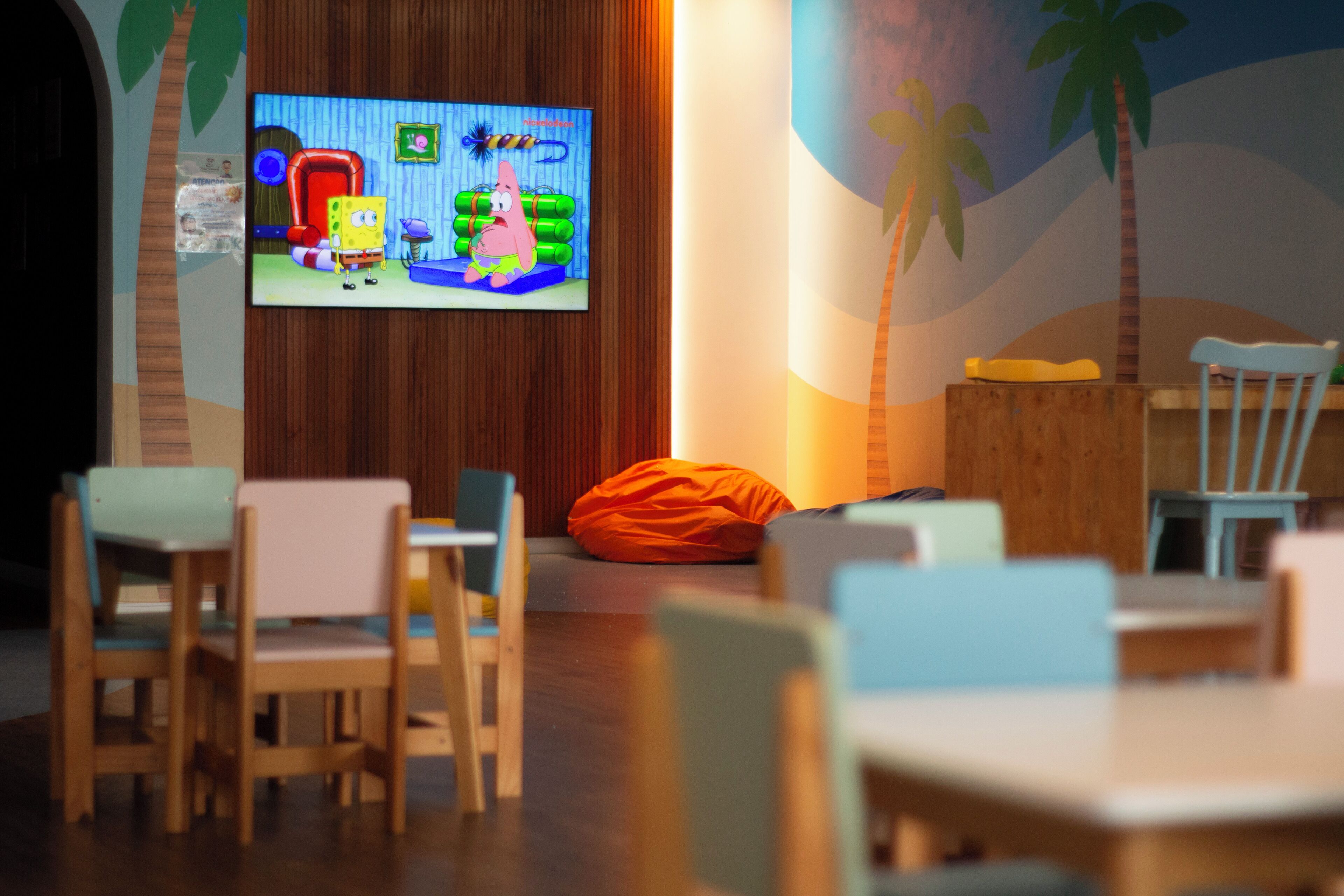 A room with wooden walls, a television displaying SpongeBob SquarePants, and a beach-themed mural.