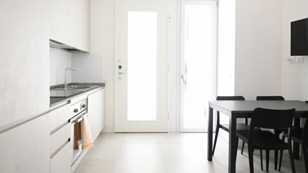 A modern kitchen with white cabinets, a stainless steel stove, and a dining area with a table and chairs. -  SE192 - Senigallia, new two-room apartment 50 meters from the sea (Senigallia)